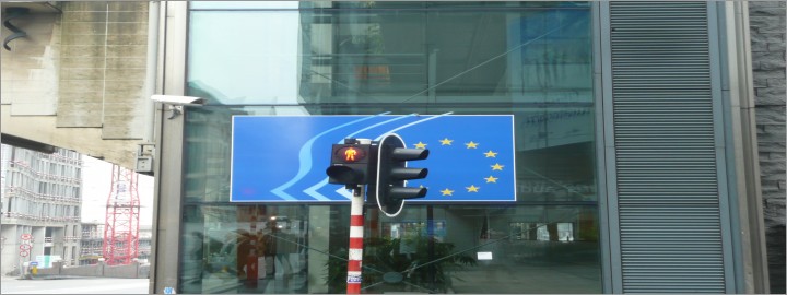 Na obrazku semafor z czerwonym światłem na tle flagi UE